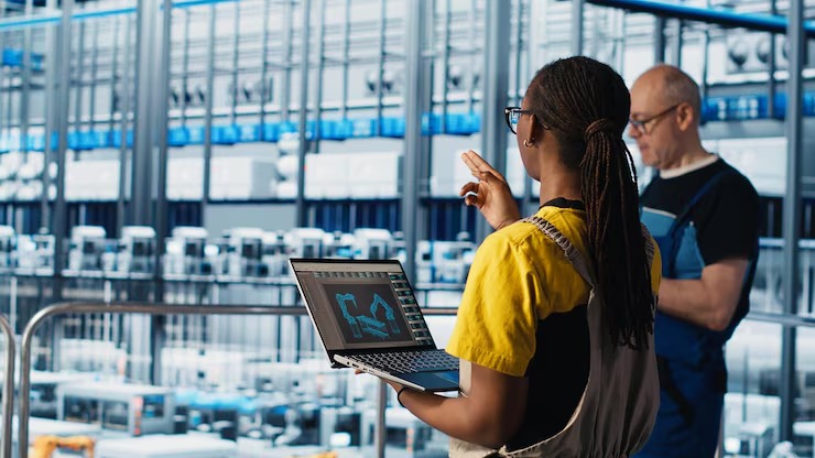 Factory workers analysing production data on laptop in industrial facility